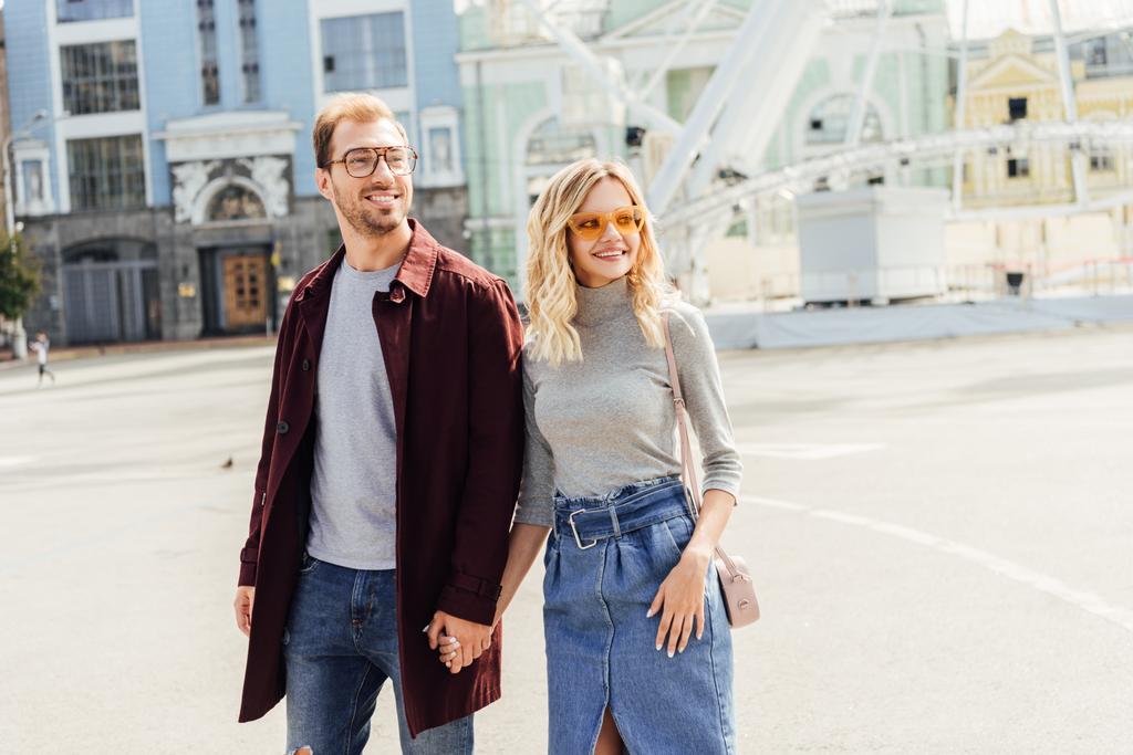sorridente coppia romantica in abito autunnale tenendosi per mano e passeggiando in città
 - Foto, immagini