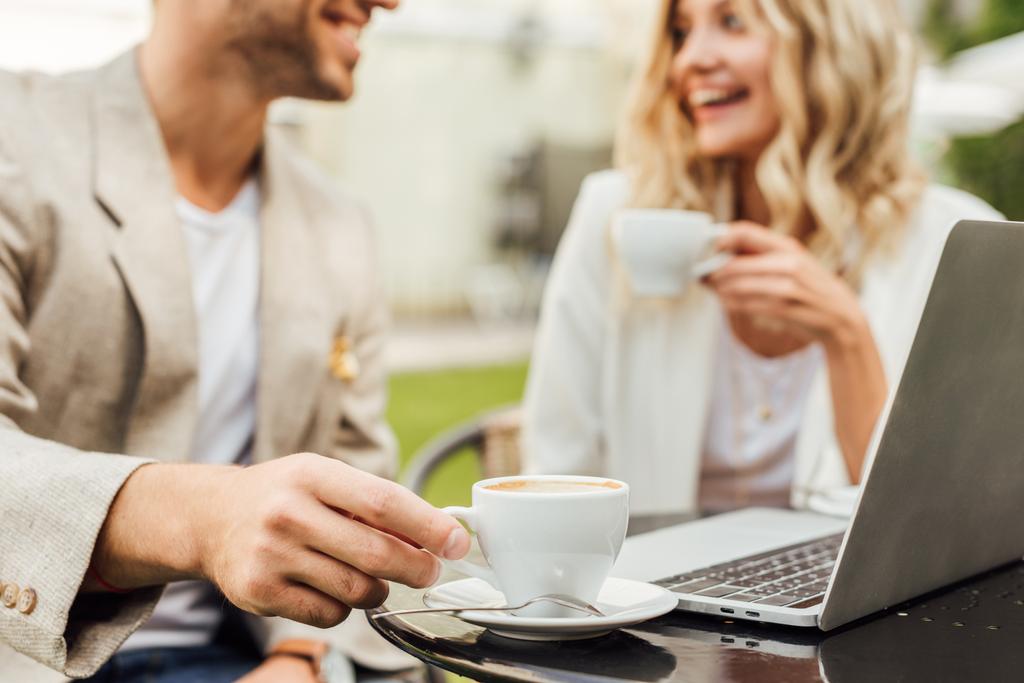 imagen recortada de pareja en traje de otoño sentado en la mesa con el ordenador portátil y beber café en la cafetería
 - Foto, imagen