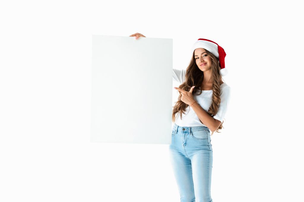 smiling girl in santa hat pointing at blank empty board, isolated on white - Photo, Image