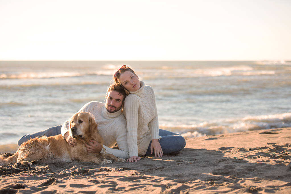 Paar mit Hund genießt am Herbsttag die gemeinsame Zeit am Strand - Foto, Bild