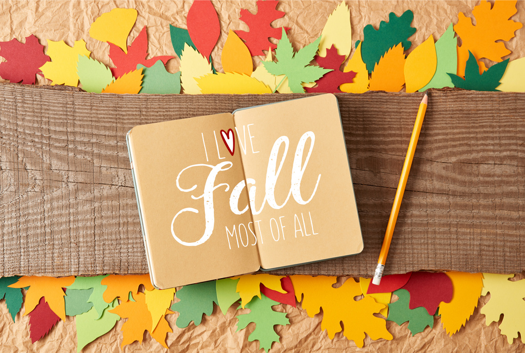 flat lay with "I love fall most of all" inspiration in notebook, pencil on wooden plank and colorful handcrafted paper leaves on crumpled paper background - Photo, Image