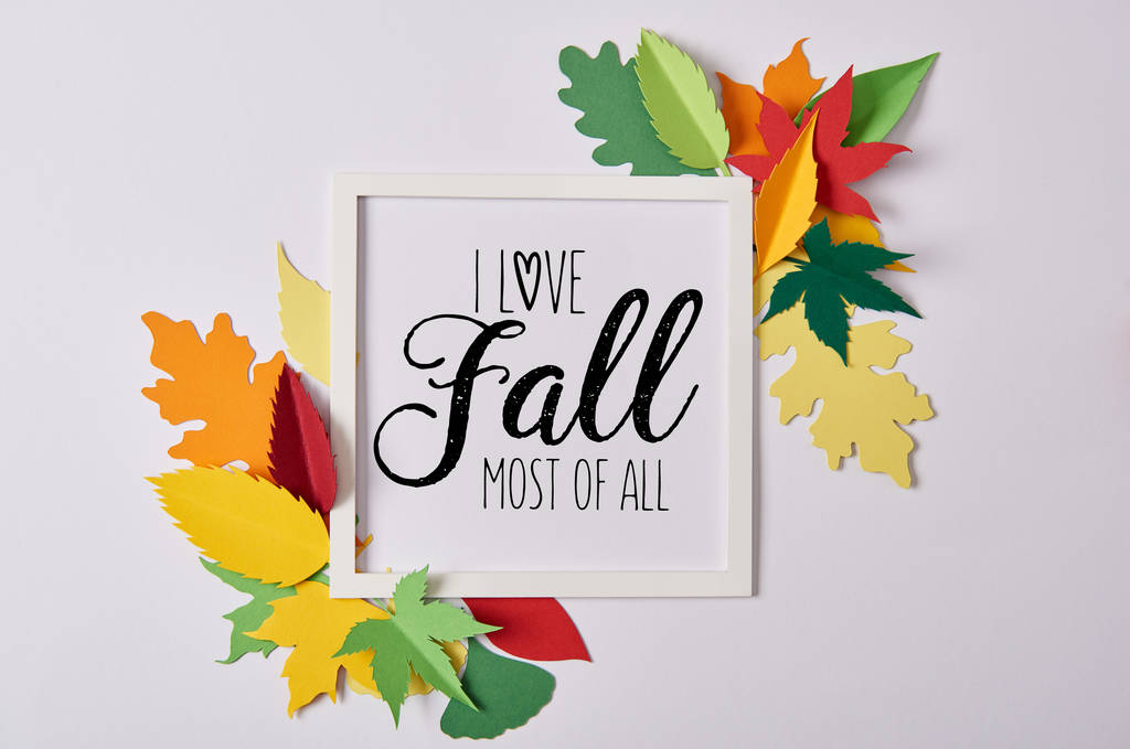 flat lay with handcrafted paper leaves and empty frame with "I love fall most of all" inspiration on white table  - Photo, Image