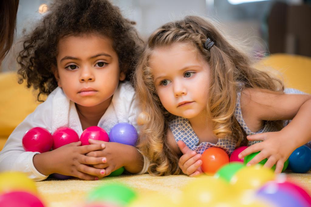 adorables niños multiculturales acostados con bolas de colores en el jardín de infantes
 - Foto, Imagen