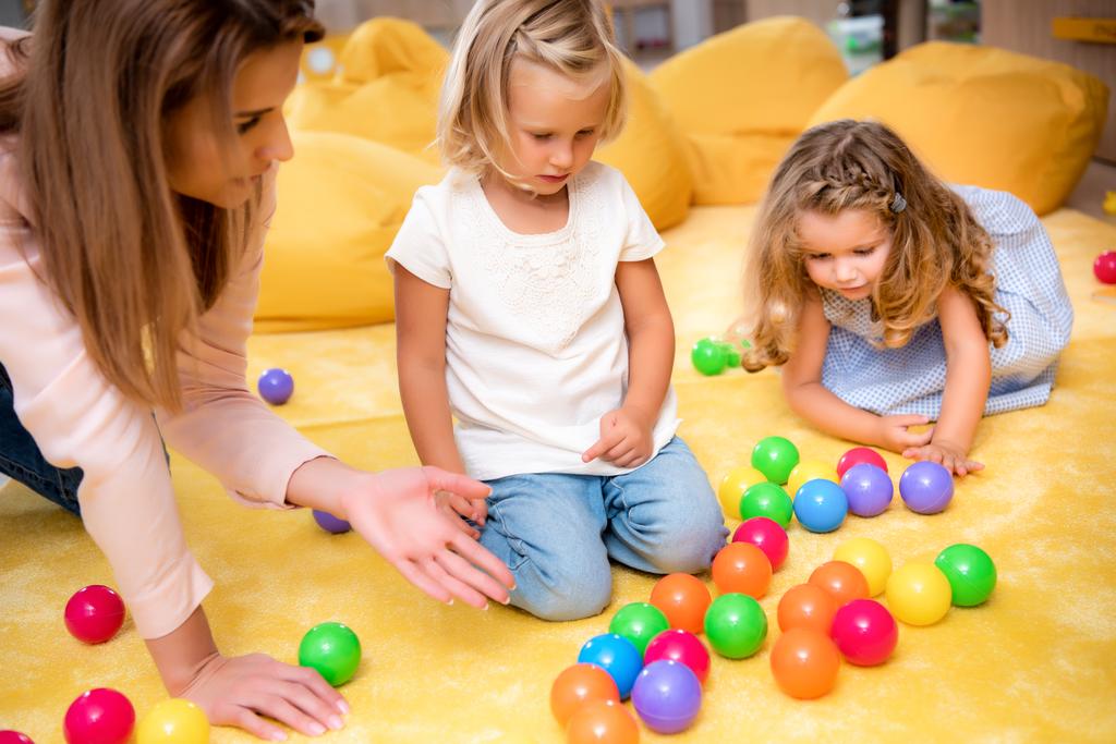 opettaja osoittaa värillisiä palloja lapsille päiväkodissa
 - Valokuva, kuva
