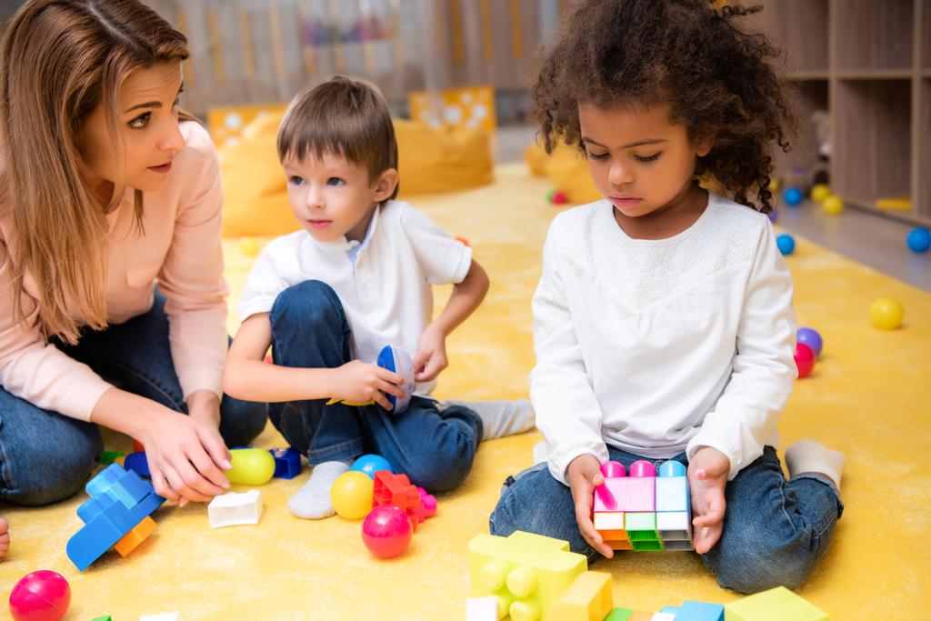 педагог і багатоетнічні діти, які грають з пластиковим конструктором в дитячому саду
 - Фото, зображення