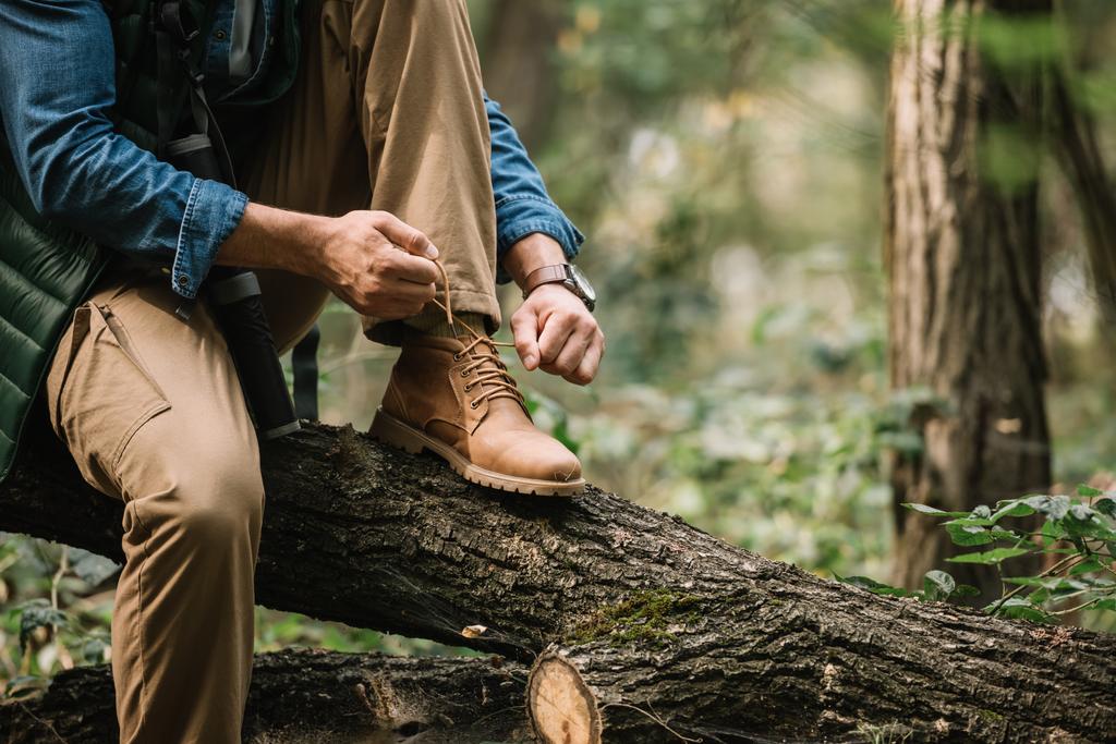 Teilansicht eines Mannes, der Schnürsenkel an Baumstamm bindet, während er allein im Wald wandert - Foto, Bild