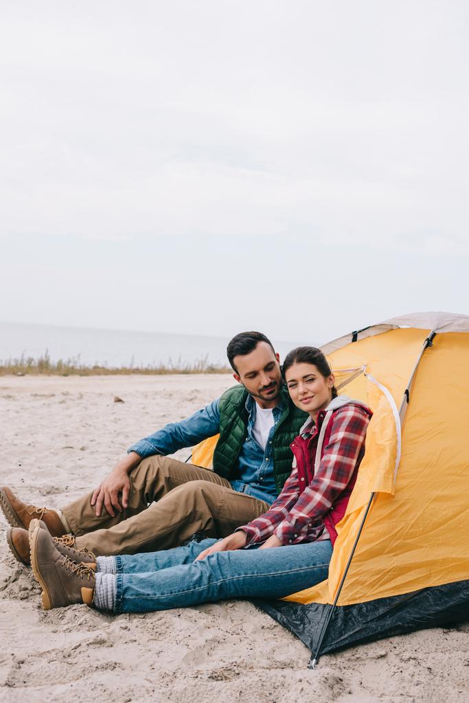 砂浜でキャンプのテントに座っているカップルの側面図 - 写真・画像