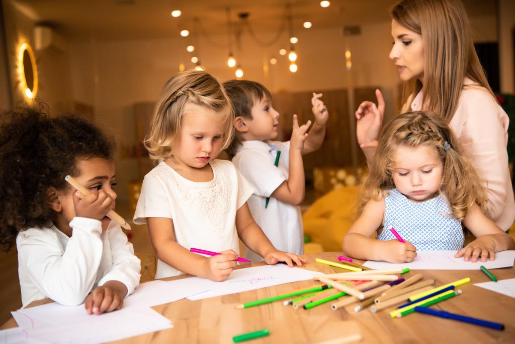 bambini multiculturali disegno nella scuola materna, educatore guardando ragazzo gestuale
 - Foto, immagini