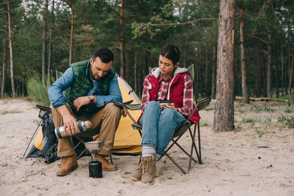 pareja teniendo camping en playa de arena con bosque de pinos detrás
 - Foto, Imagen