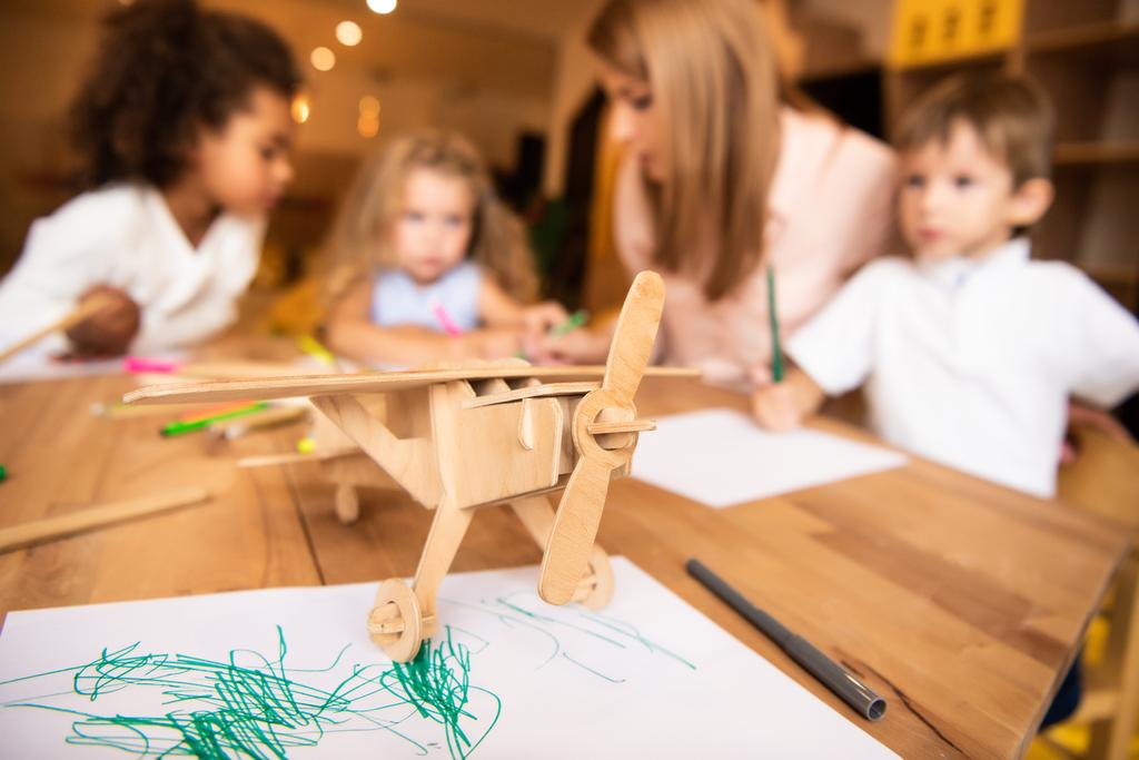 Erzieherin und multikulturelle Kinder zeichnen im Kindergarten, Holzfläche im Vordergrund - Foto, Bild