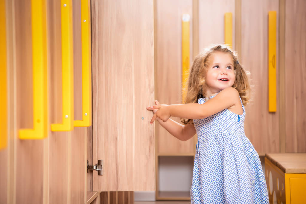 lächelndes entzückendes Kind öffnet Spind in Kindergarten-Garderobe - Foto, Bild