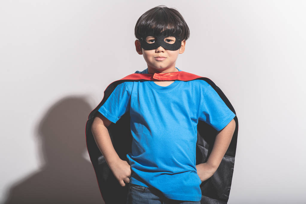 Young Boy Superhelden Porträt in weißem Hintergrund mit hartem Licht. Mischlingsjunge in blauem Hemd, Jeans, Maske, Umhang. bereit zum Kampf. - Foto, Bild