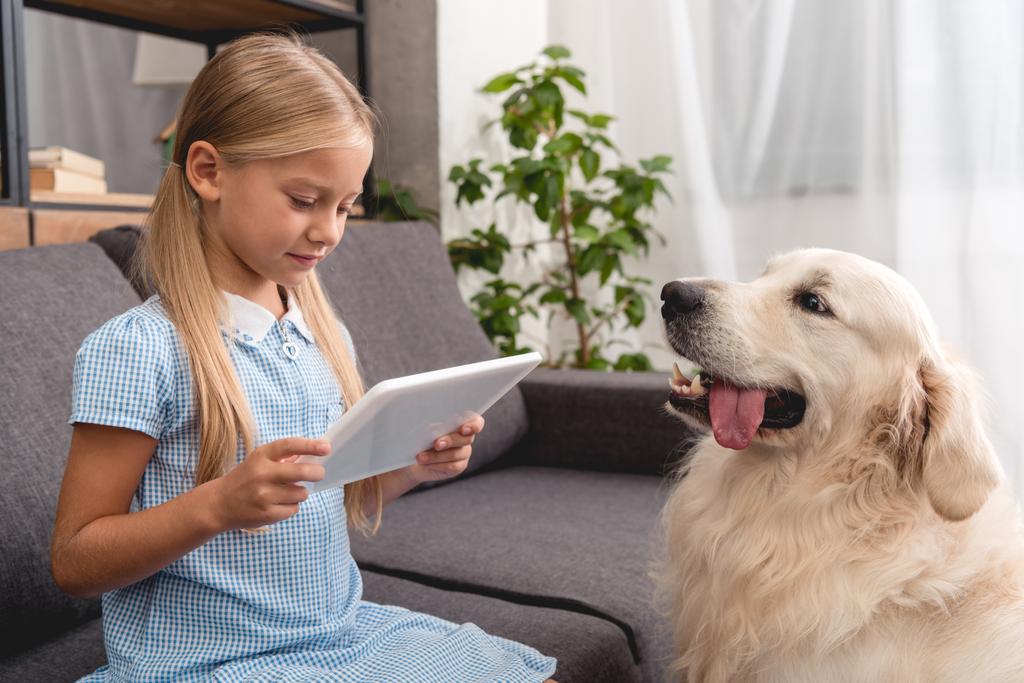 sevimli küçük çocuk ile labrador köpek kanepede otururken tablet kullanma - Fotoğraf, Görsel