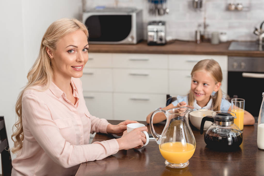 Gelukkig jonge moeder en dochter samen ontbijten op keuken - Foto, afbeelding