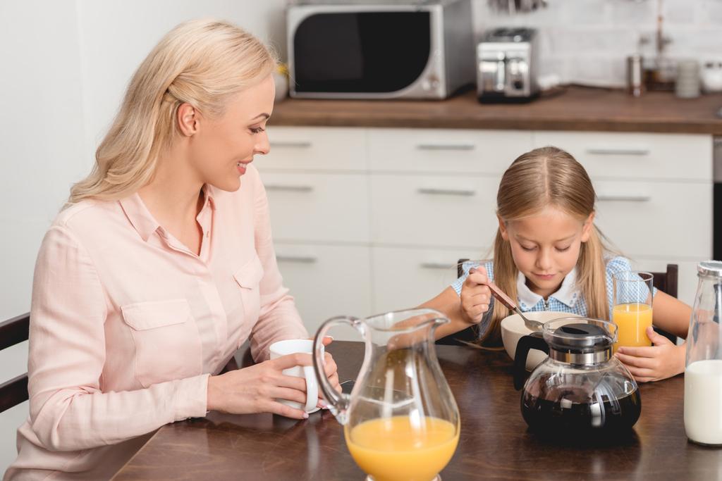 smiling mother and daughter having breakfast together on kitchen - Photo, Image