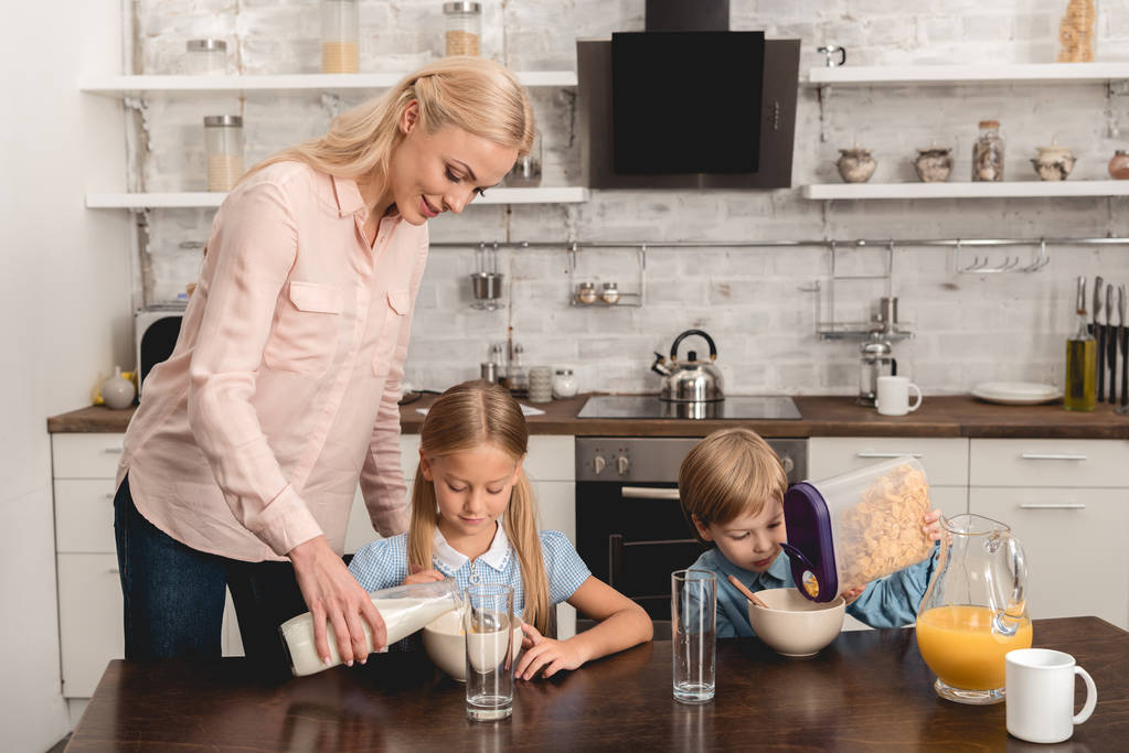 мати вливає молоко в крупу для чарівних маленьких дітей під час сніданку
 - Фото, зображення