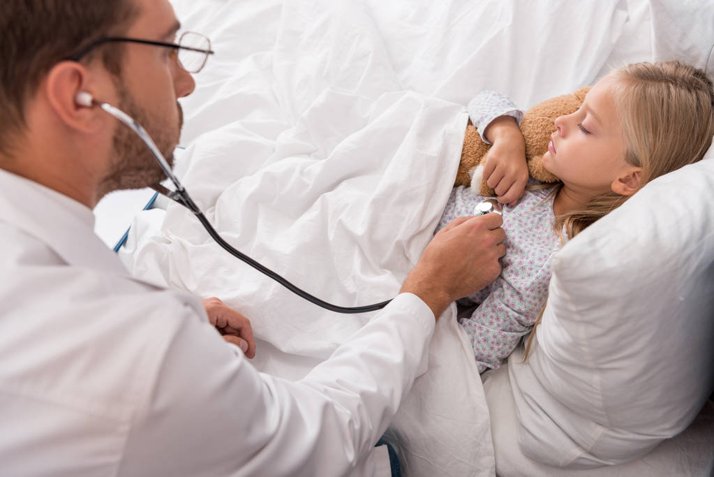 high angle view of pediatrician litening childs breath with stethoscope while she lying in bed - Photo, Image