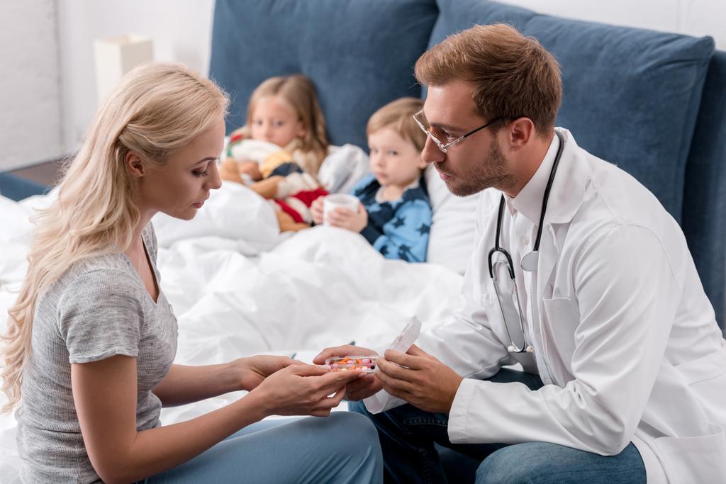pediatra dando pastillas a la madre de los niños enfermos acostados en la cama sobre el fondo
 - Foto, imagen