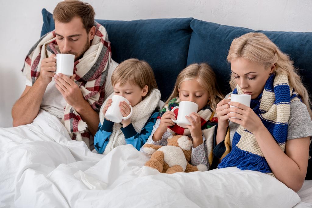 ベッドに座りながら地球温暖化飲料を飲んで病気の若い家族 - 写真・画像