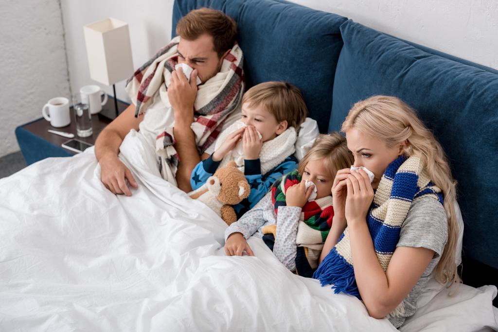 hoge hoekmening van ziek jong gezin waait neus met servetten samen terwijl liggend in bed - Foto, afbeelding