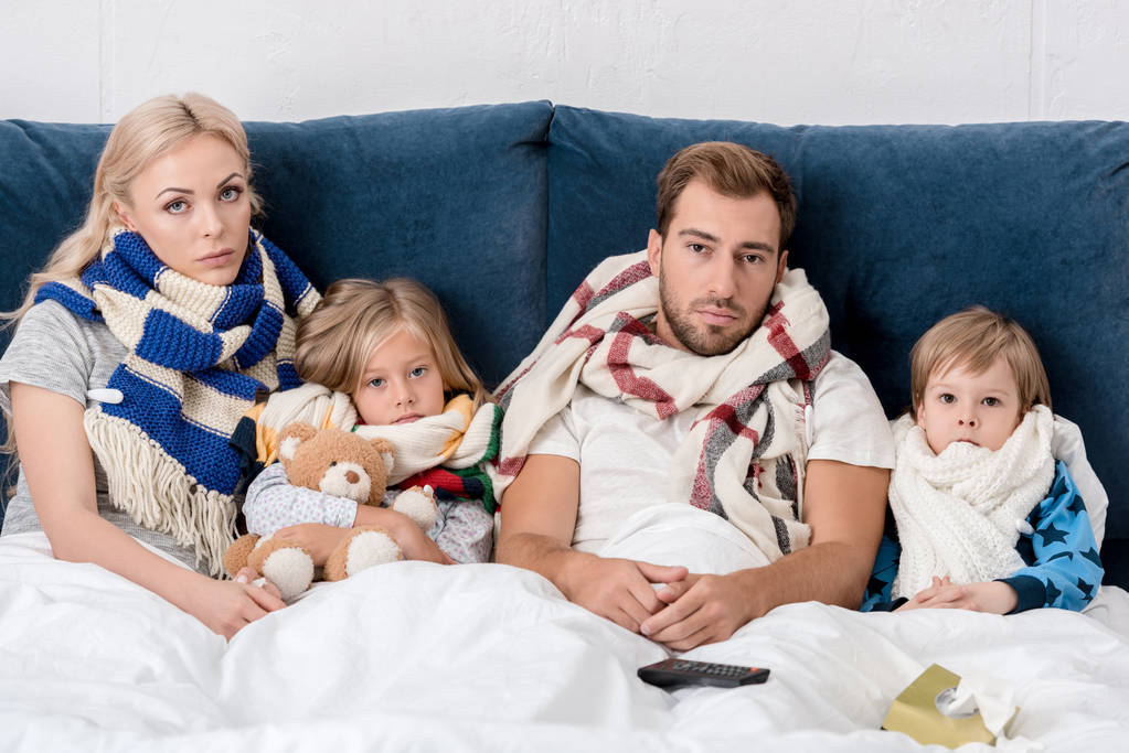 ziek jong gezin in sjaals camera kijken terwijl liggend in bed - Foto, afbeelding
