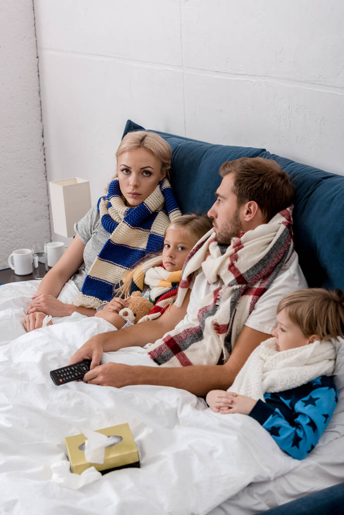 sick young family in scarves lying in bed together - Photo, Image
