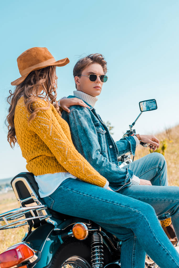 junges Paar sitzt auf Motorrad und entspannt auf ländlicher Wiese - Foto, Bild