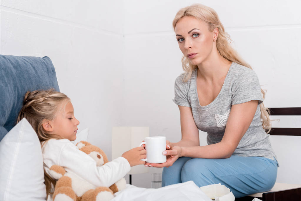 jeune mère donnant tasse de thé chaud à sa fille malade au lit
 - Photo, image