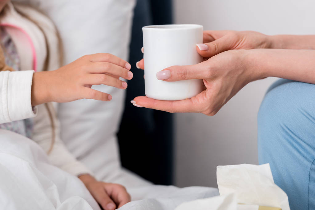 recortado disparo de la madre dando taza de té caliente a su hija enferma en la cama
 - Foto, Imagen