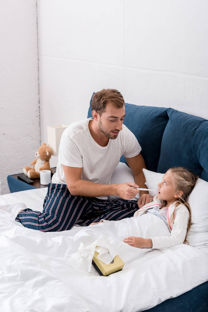 joven padre comprobar hijas oral temperatura mientras ella acostado en cama
 - Foto, Imagen