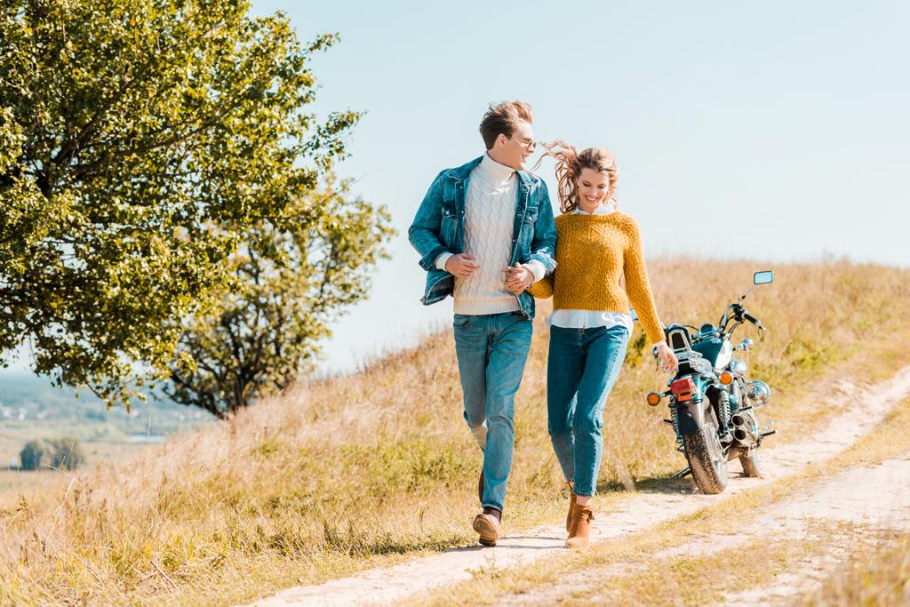 Glückliches Paar läuft mit Motorrad im Hintergrund über Wiese - Foto, Bild