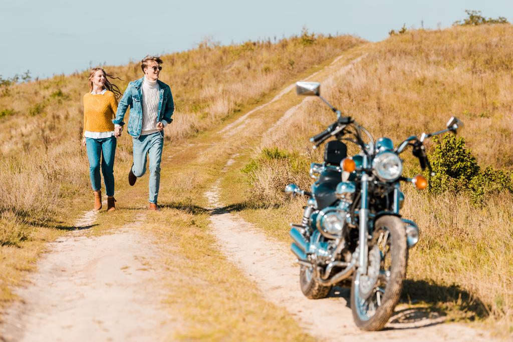 junges Paar rennt auf Bauernwiese zu Motorrad - Foto, Bild