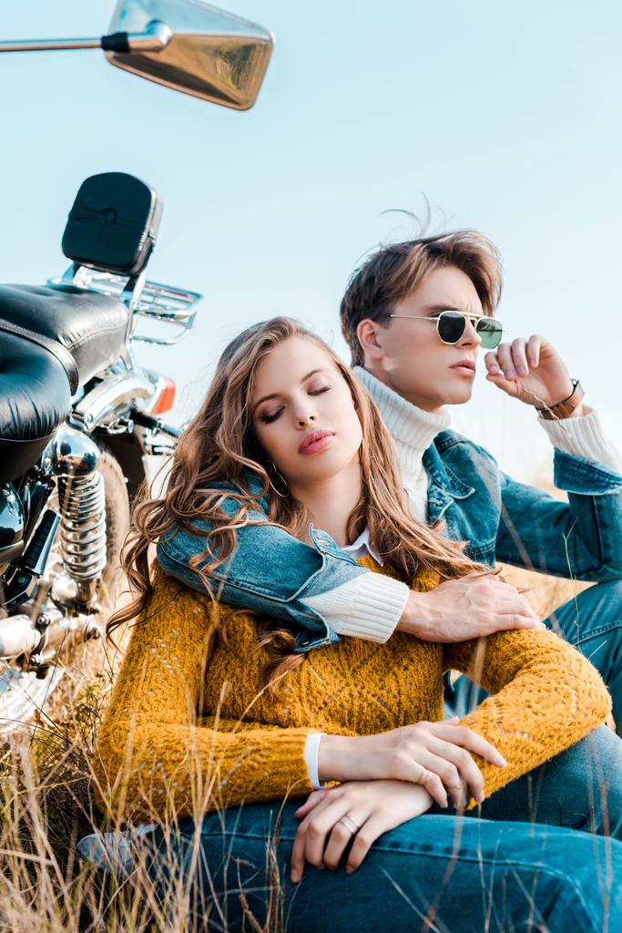 молодой парень обнимает девушку и сидит рядом с винтажным мотоциклом
 - Фото, изображение