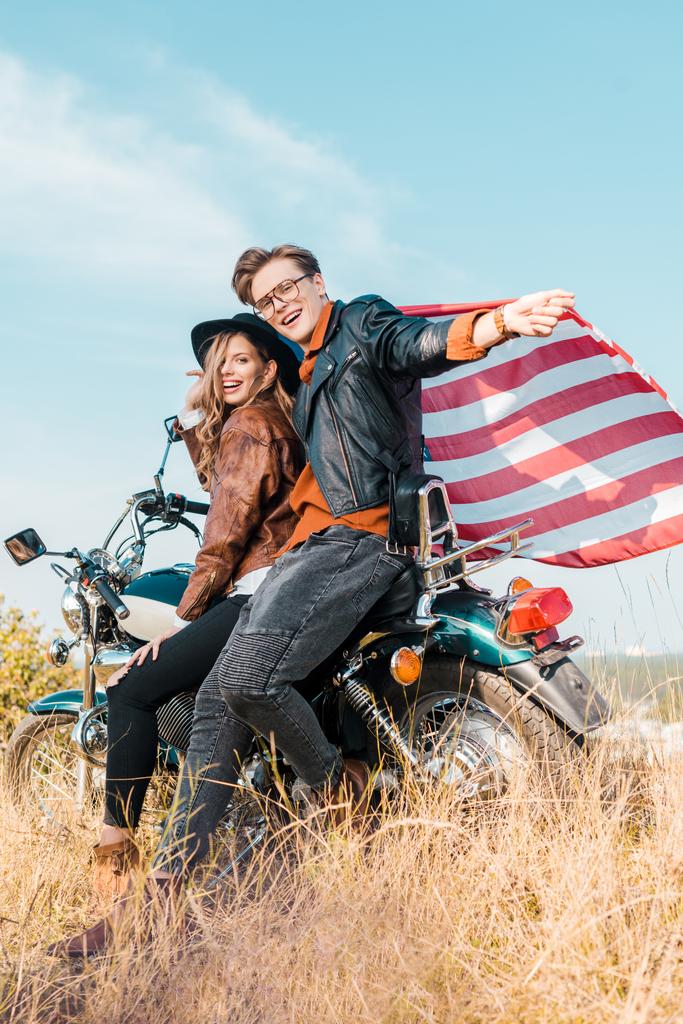 jovem casal sorridente com bandeira americana sentado em moto, conceito dia de independência
   - Foto, Imagem