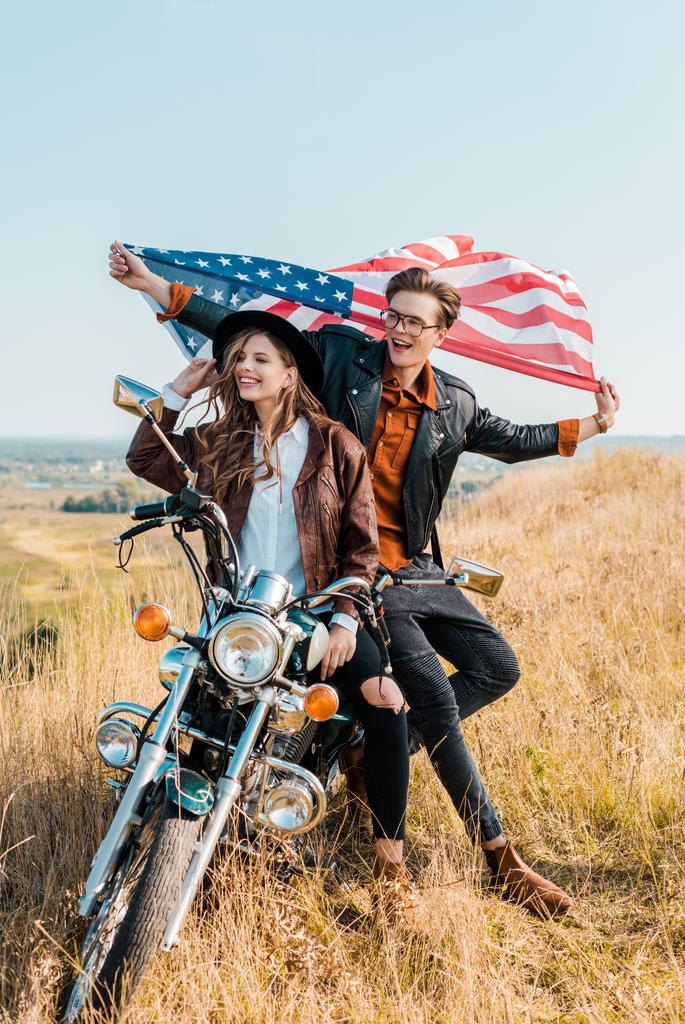 Lächelndes Paar mit amerikanischer Flagge auf Motorrad, Konzept zum Unabhängigkeitstag   - Foto, Bild