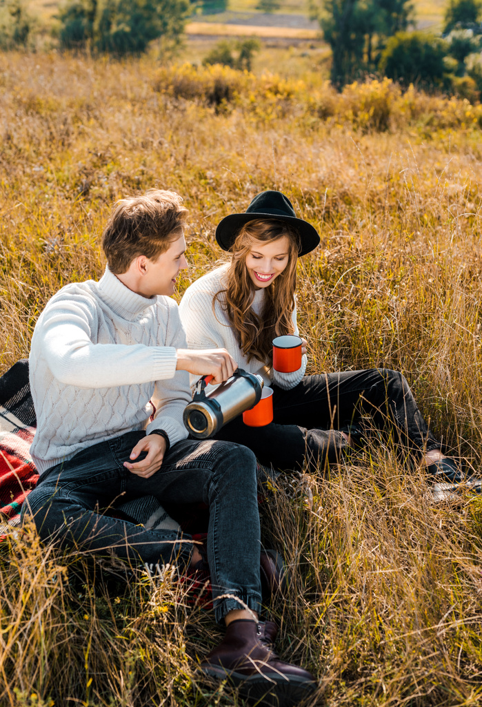счастливая пара наливает горячий напиток из термоса и отдыхает на сельском лугу
 - Фото, изображение