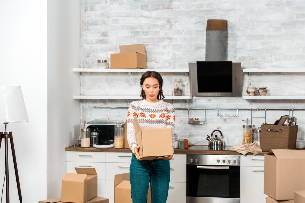 mujer joven sorprendida mirando en la caja de cartón en la cocina en el nuevo hogar
  - Foto, imagen