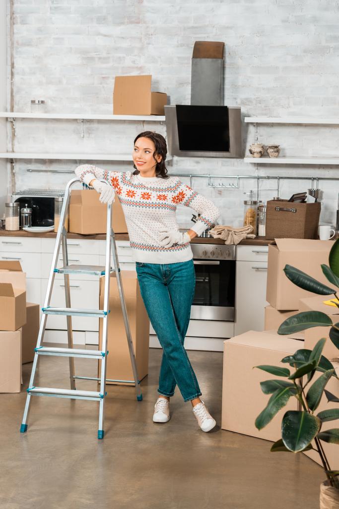 молода жінка в робочих рукавичках стоїть біля сходів на кухні з картонними коробками в новому будинку
  - Фото, зображення