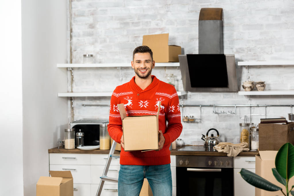 smiling man with cardboard box in kitchen with cardboard boxes during relocation in new home  - Photo, Image
