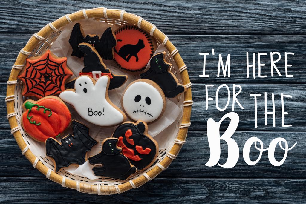 bovenaanzicht van rieten mand met zelfgemaakte spooky halloween cookies op houten tafel met "Im hier voor de Boo" belettering - Foto, afbeelding