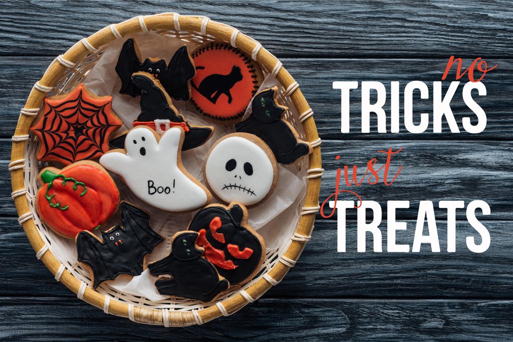 top view of wicker basket with homemade spooky halloween cookies on wooden table  with "no tricks just treats" lettering - Photo, Image