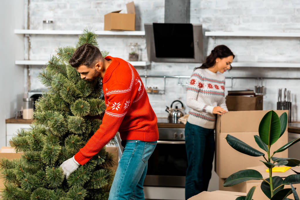 a fiatalember üzembe karácsonyfa, míg a barátnője mögött otthon a konyhában  - Fotó, kép