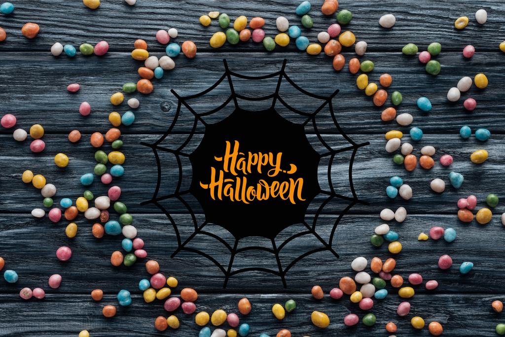 Kreis aus bunten leckeren Bonbons auf hölzernem Hintergrund mit Spinnennetz und "Happy Halloween" -Schriftzug - Foto, Bild