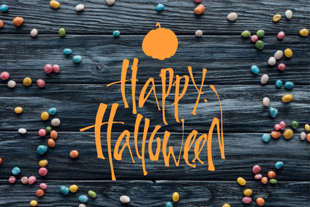 erhöhte Ansicht der arrangierten bunten leckeren Bonbons auf hölzernem Hintergrund mit Kürbis und "Happy Halloween" -Schriftzug - Foto, Bild