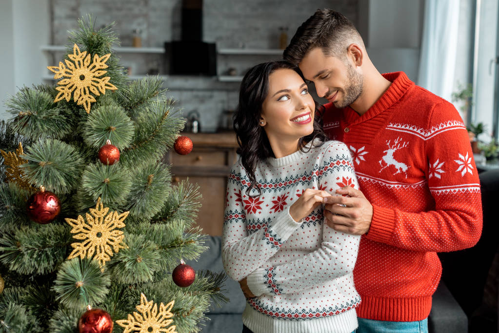 mosolygó fiatal pár átfogó és néztek egymásra, otthon a karácsonyfa közelében - Fotó, kép
