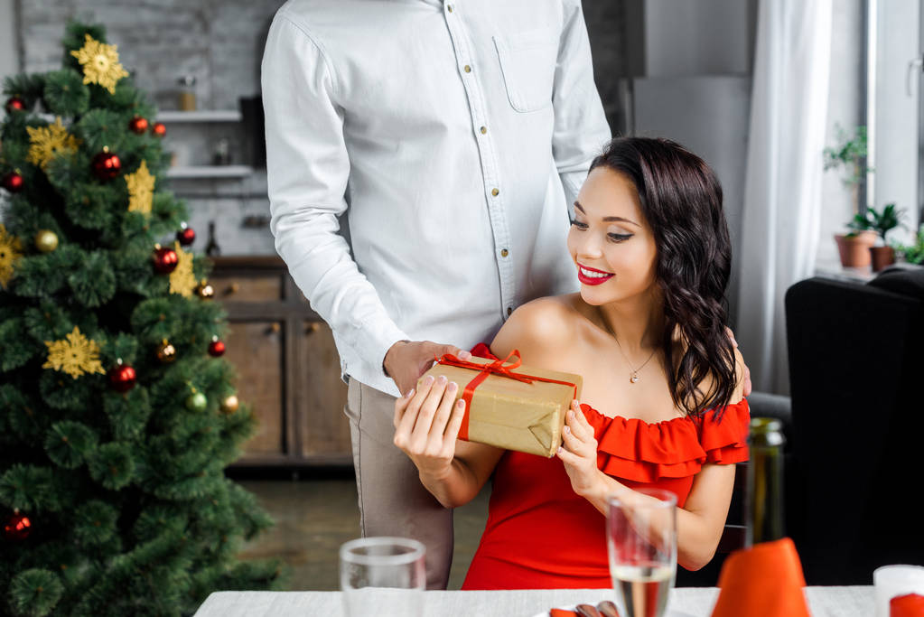 vue partielle de l'homme cadeau boîte cadeau à petite amie souriante assis à la table servie à la maison
  - Photo, image