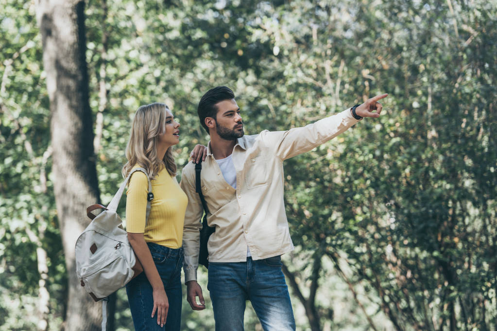 junges verliebtes Paar mit Rucksäcken im Park, Mann zeigt weg - Foto, Bild