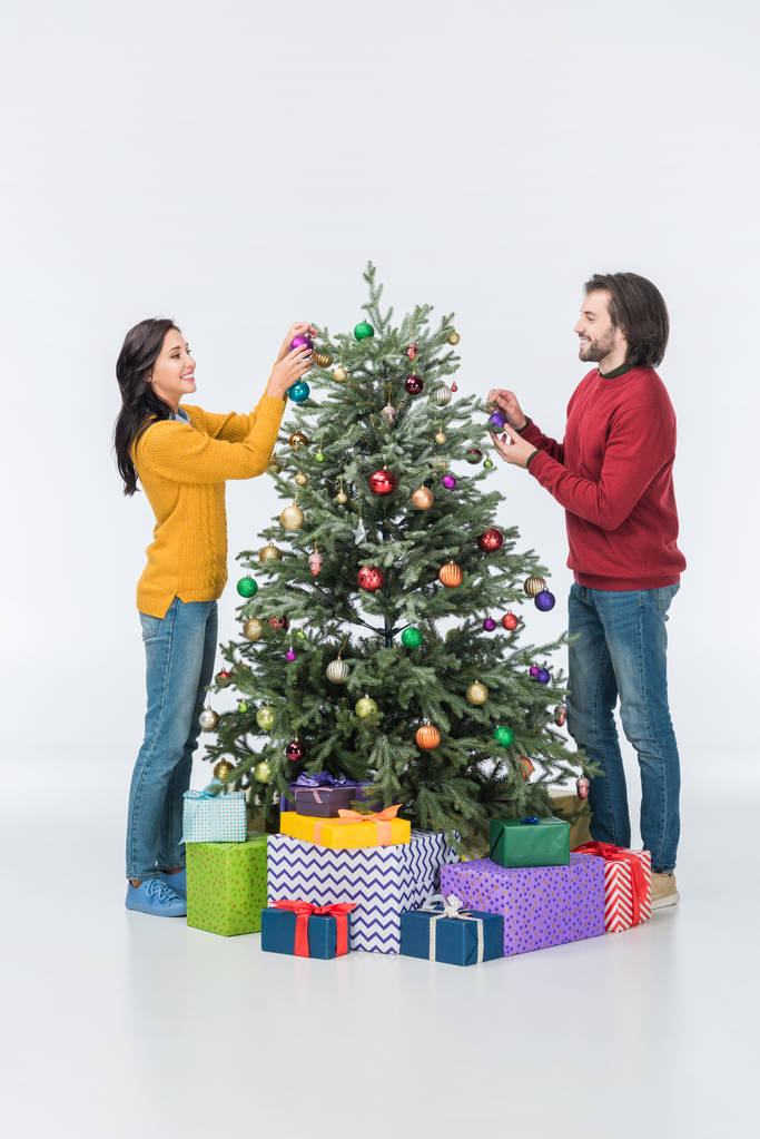 Lächelndes Paar schmückt Weihnachtsbaum mit Glaskugeln isoliert auf Weiß - Foto, Bild
