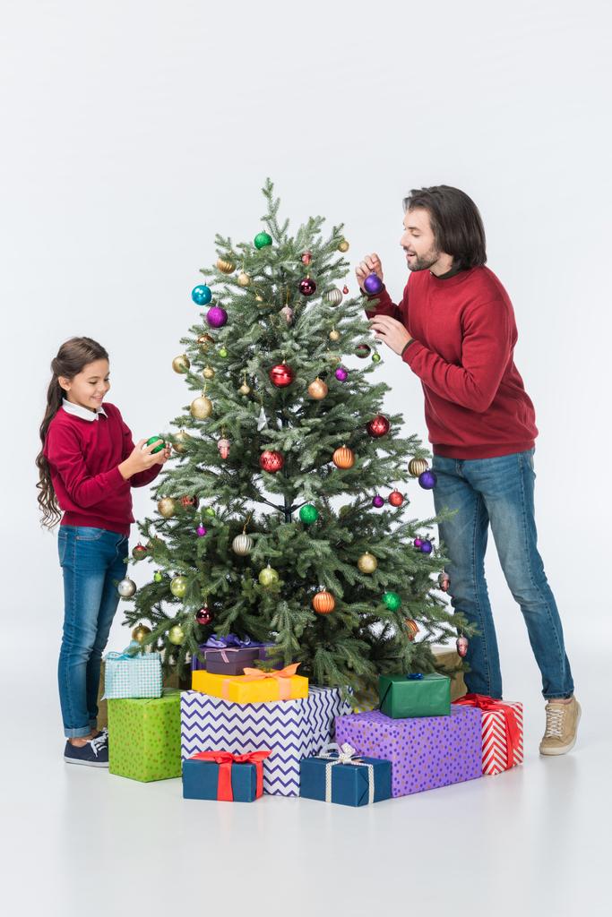 Feliz padre mirando a su hija decorando el árbol de Navidad con bolas de vidrio aisladas en blanco
 - Foto, Imagen