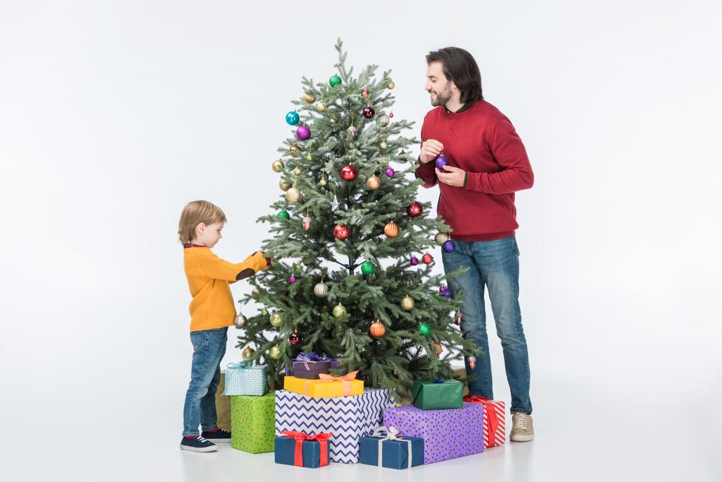 Vater mit Sohn schmückt Weihnachtsbaum mit Glaskugeln und Geschenken isoliert auf Weiß - Foto, Bild